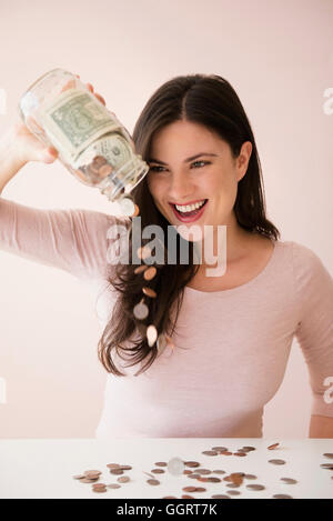 Caucasian woman pouring jar of money onto table Stock Photo