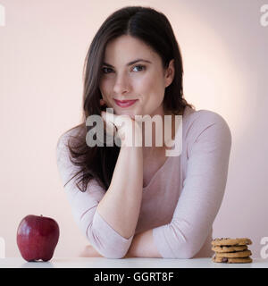 Caucasian woman choosing between apple or cookies for snack Stock Photo
