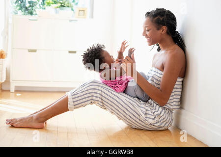 Black woman sitting on floor clapping hands with baby daughter Stock Photo