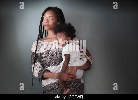 Thoughtful Black woman standing holding baby daughter Stock Photo