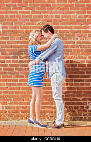 Smiling Caucasian man and expectant mother hugging near red brick wall Stock Photo