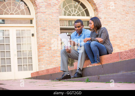 Couple sitting on steps reading paperwork Stock Photo