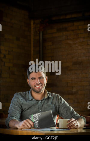 Caucasian man drinking coffee in cafe holding booklet Stock Photo