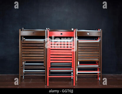Folding colorful wooden chairs standing at the black wall at the school after classes. Stock Photo