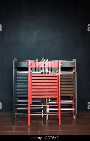 Folding colorful wooden chairs standing at the black wall at the school after classes. Stock Photo