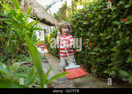 Caucasian boy playing with broom on path near house Stock Photo