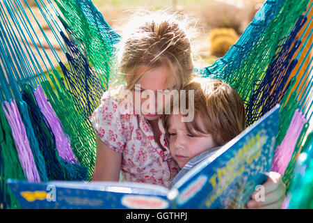 Caucasian sister reading book to brother in hammock Stock Photo