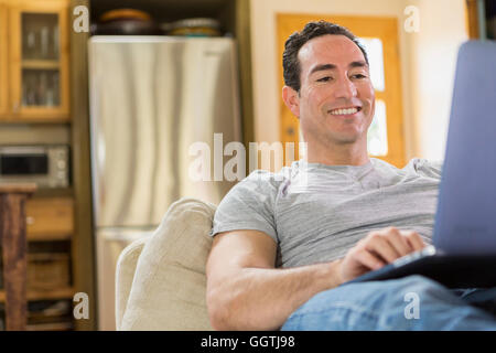 Hispanic man laying on sofa using laptop Stock Photo