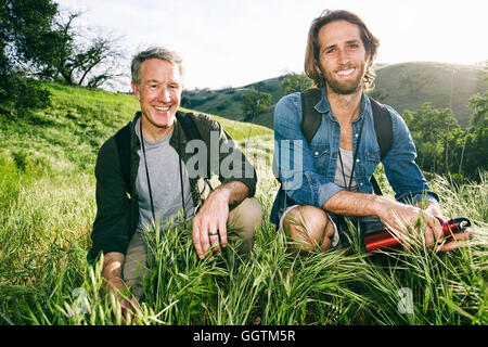 Caucasian hikers crouching in grass on mountain Stock Photo