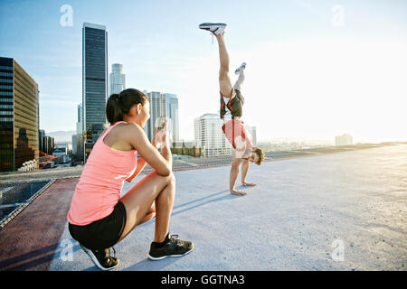 Woman photographing man doing handstand on urban rooftop Stock Photo