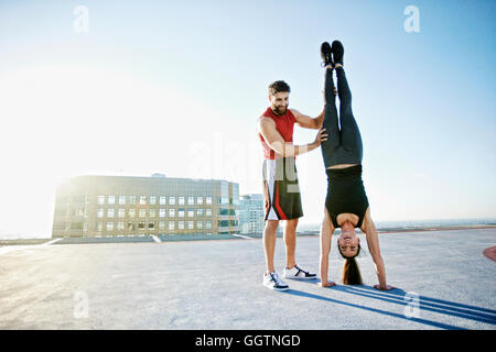 Caucasian man helping woman do handstand on urban rooftop Stock Photo