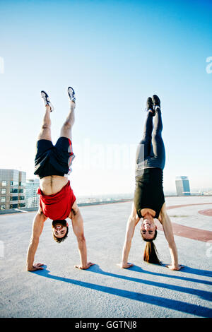 Caucasian couple doing handstands on urban rooftop Stock Photo