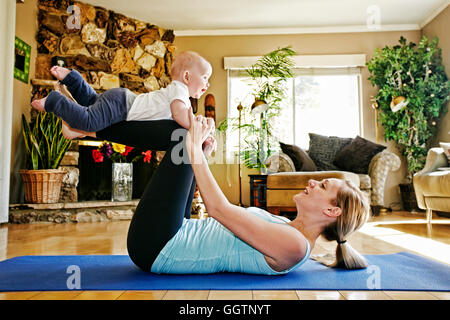 Mother working out on exercise mat balancing baby on legs Stock Photo