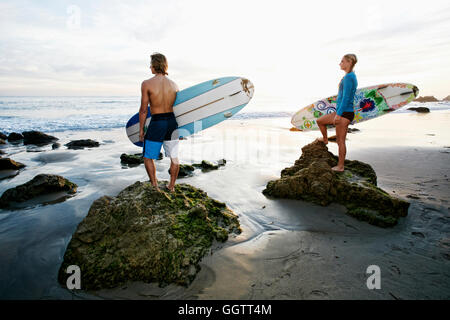 Caucasian couple standing on rocks carrying surfboards at beach Stock Photo