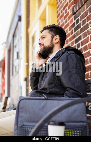 Hispanic man sitting on city bench using cell phone Stock Photo