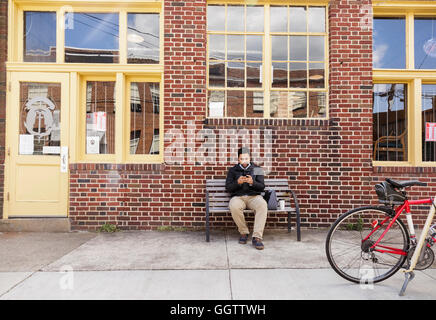 Hispanic man sitting on city bench using cell phone Stock Photo