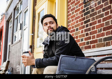 Hispanic man sitting on city bench drinking coffee Stock Photo