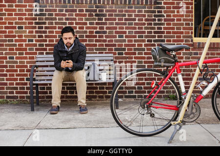 Hispanic man sitting on city bench using cell phone Stock Photo