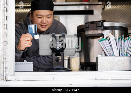 Asian man processing credit card using digital tablet at food cart Stock Photo