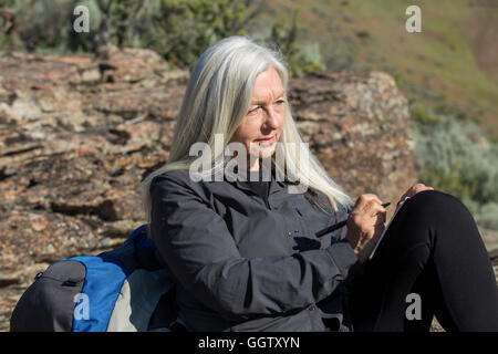 Older Caucasian woman leaning on rock writing in journal Stock Photo