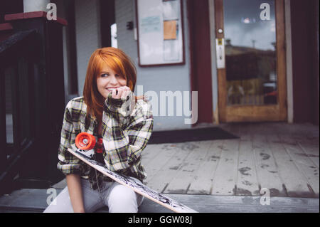 Caucasian woman holding skateboard on patio Stock Photo