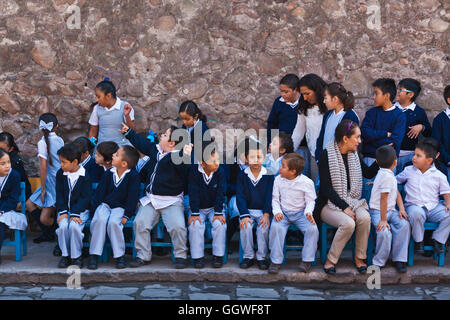 School children watch the parade celebrating DAY OF THE REVOLUTION on November 20th each year - SAN MIGUEL DE ALLENDE, MEXICO Stock Photo