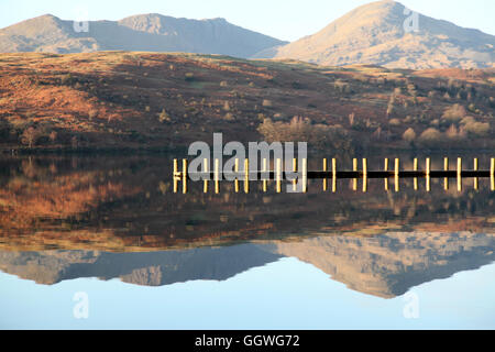 A wooden jetty crosses the reflection of a Lakeland mountain on Coniston water in winter Stock Photo