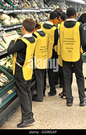 Group of school children in uniform wearing high visibility bibs on trip to local Tesco supermarket interior to learn about the UK food supply chain Stock Photo
