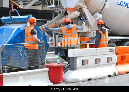 Labourer on City of London England UK building site helps delivery cement mixer truck reverse to crane hopper for unloading readymix concrete lorry Stock Photo