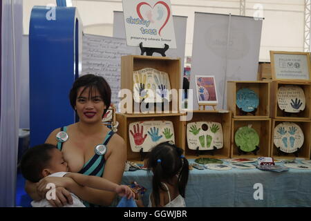 Mom breastfeeds her 4 year old while this young girl looks at her items from her small business. To celebrate the National Breastfeeding Awareness Month in August, the online support group of over 100,000 mothers called “Breastfeeding Pinays” is hosting Hakab Na! 2016. Simultaneous Breastfeeding Central to the event celebrations on August 6 is the act of mothers simultaneously breastfeeding their children as part of The Big Latch On, an international activity where mothers latch on their babies from different locations around the world to create a world record. The event logged a total of 1, 8 Stock Photo