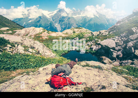Man laying relaxing with backpack on rocks Travel Lifestyle concept serene view of mountains landscape summer vacations outdoor Stock Photo