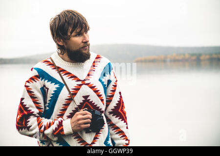 Young Man bearded with retro photo camera Fashion Travel Lifestyle wearing knitted sweater clothing outdoor foggy nature on back Stock Photo