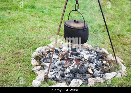 Large black cast iron pot cooking over open fire at campsite. Stock Photo