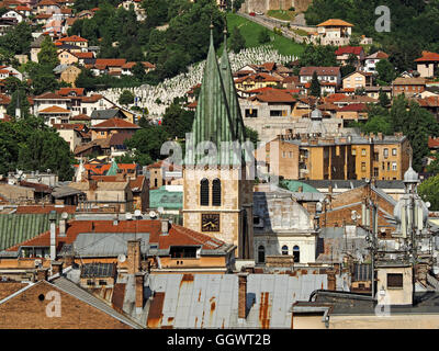 view over Sarajevo rooftops to twin bell towers of Cathedral of Jesus's Sacred Heart with one of many graveyards in distance Stock Photo