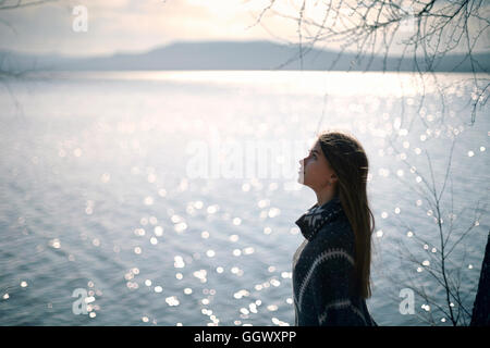 Pensive Caucasian girl at lake looking up Stock Photo