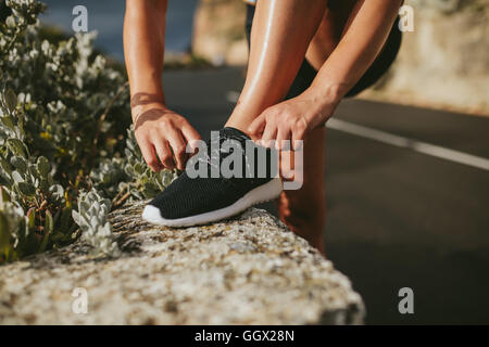 Woman lacing running shoes before workout outdoors on countryside road. fitness and healthy lifestyle concept. Stock Photo