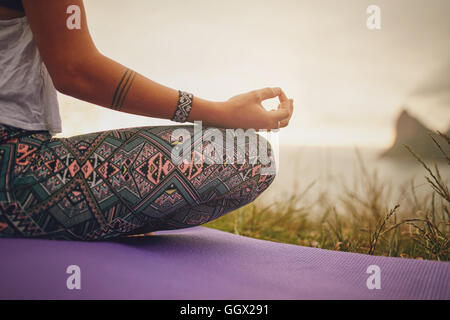 Cropped shot of woman sitting in lotus yoga pose on exercise mat, with focus on hands. fitness female meditating outdoors. Stock Photo