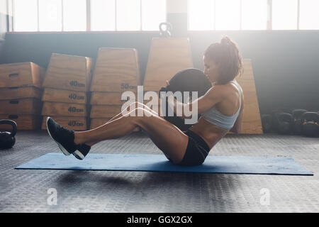 Side view shot of energetic woman doing abdominal exercise at fitness center. Woman athlete doing situps at the gym holding heav Stock Photo
