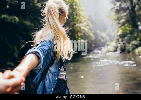 Young woman leading her boyfriend on the forest hike. Point of view shot of couple crossing the creek holding hands. Stock Photo