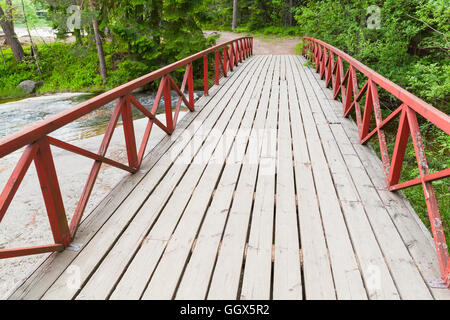 Wooden bridge with red railings over stream in summer park. Kotka, Finland Stock Photo