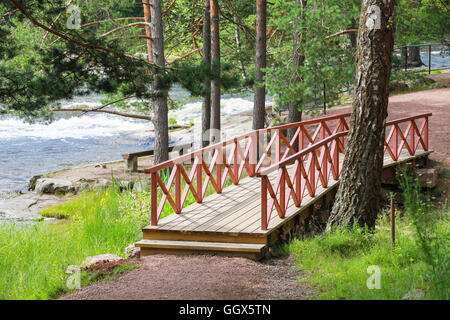 Small wooden bridge with red railings over stream in summer park. Kotka, Finland Stock Photo