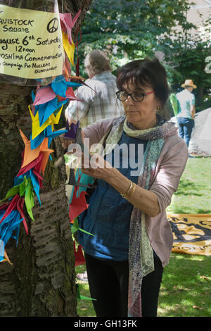 London, UK. 6th August 2016. A woman fixes peace cranes on the commemorative cherry tree at the CND ceremony in memory of the victims, past and present on the 71st anniversary of the dropping of the atomic bomb on Hiroshima and the second atomic bomb dropped on Nagasaki three days later. Peter Marshall/Alamy Live News