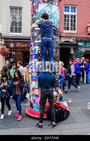 Edinburgh, Scotland, UK. 7th August, 2016. Performers from Fringe shows entertain in the High Street to promote their shows.  A performer placing a poster for his show on a pillar in the High Street Credit:  Andrew Wilson/Alamy Live News Stock Photo