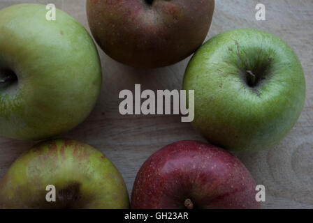 Five apples, three green and two red shaped in a round composition on a wooden board Stock Photo