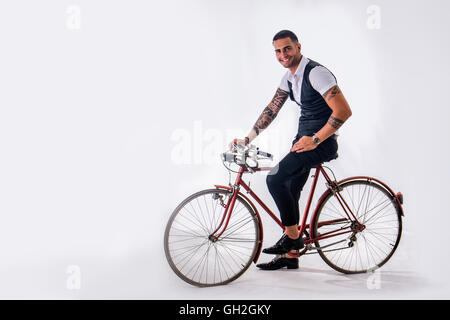 Portrait of young tattooed man in elegant clothes and shoes riding a bicycle.Isolate.Studio shot. Stock Photo