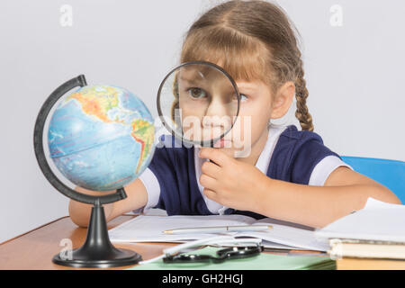 Schoolgirl looking at globe through a magnifying glass Stock Photo