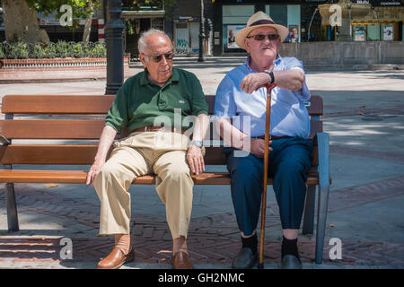 Two senior citizen men sit on a plaza bench and relax during the day in Granada, Spain. Stock Photo