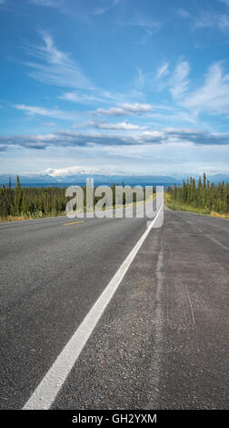 A two lane highway stretches towards distant snow capped mountain in eastern Alaska. Stock Photo