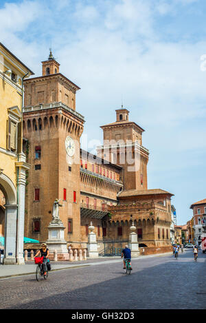 Cyclists crossing Corso Martiri della Liberta street with Estense castle in background. Ferrara, Italy. Stock Photo