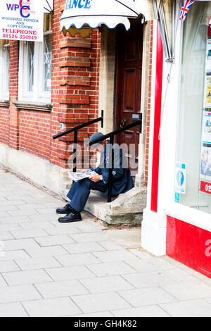 Man sat on step reading newspaper sitting down in suit on steps on street path UK England GB Stock Photo
